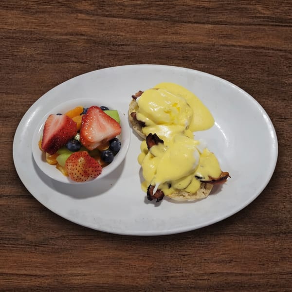 Eggs Benedict with bacon and hollandaise sauce, served with a side of fresh fruit.