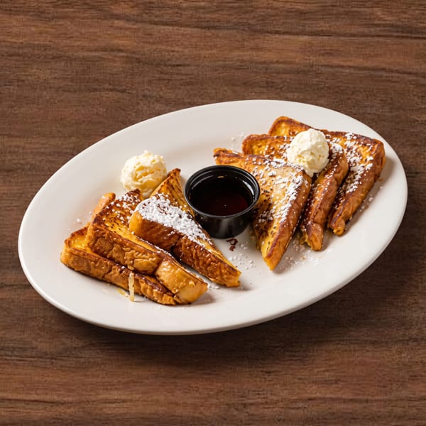 Golden french toast with powdered sugar, butter, and syrup on a white oval plate.